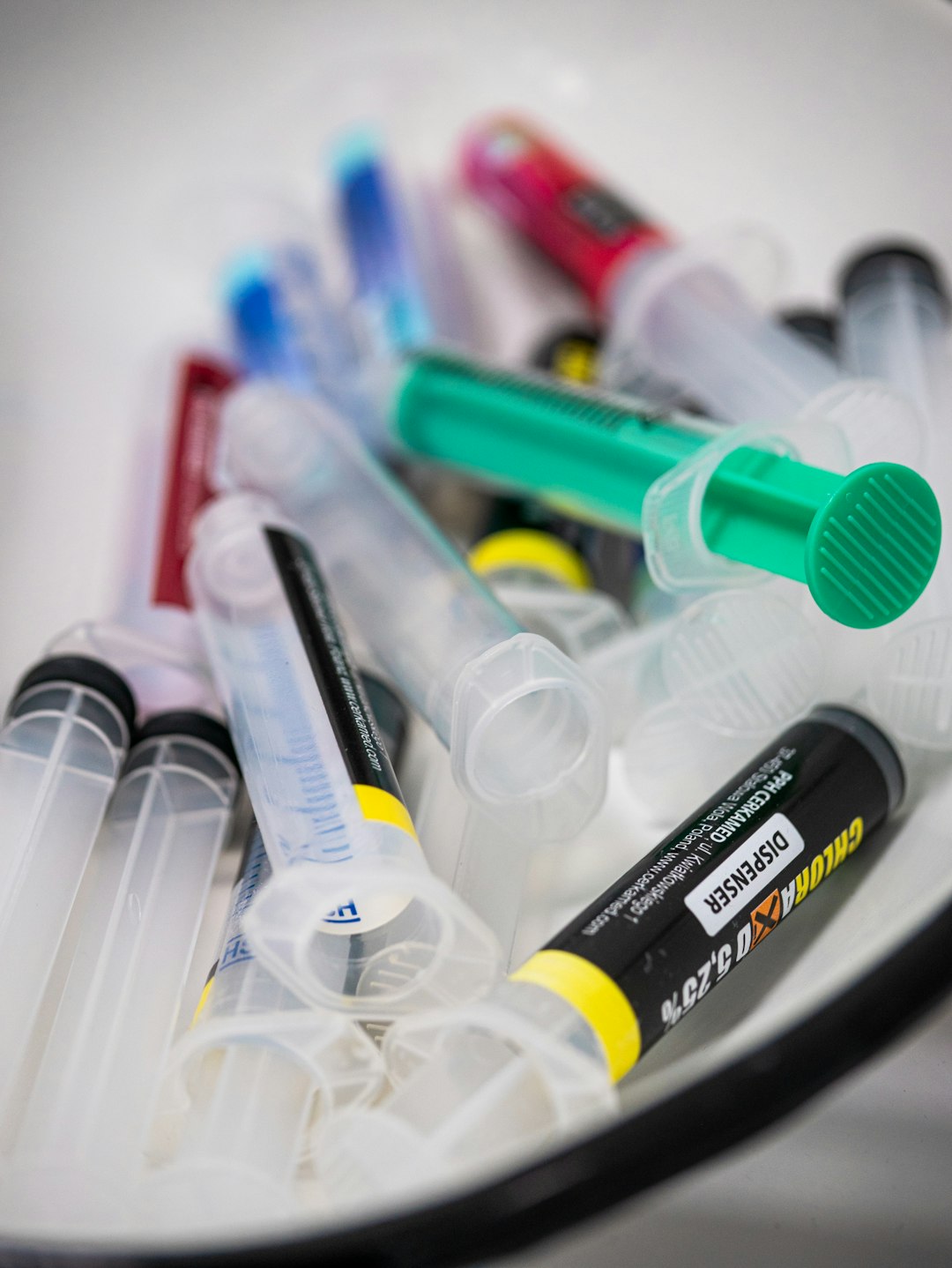 Syringes are piled together in a white container.